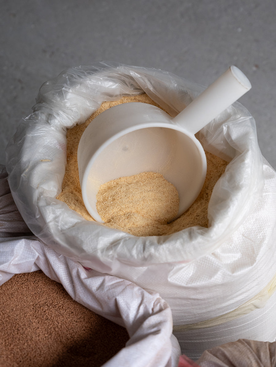 A white bag with a partially filled scoop resting on top of beige coloured bamboo fibres.