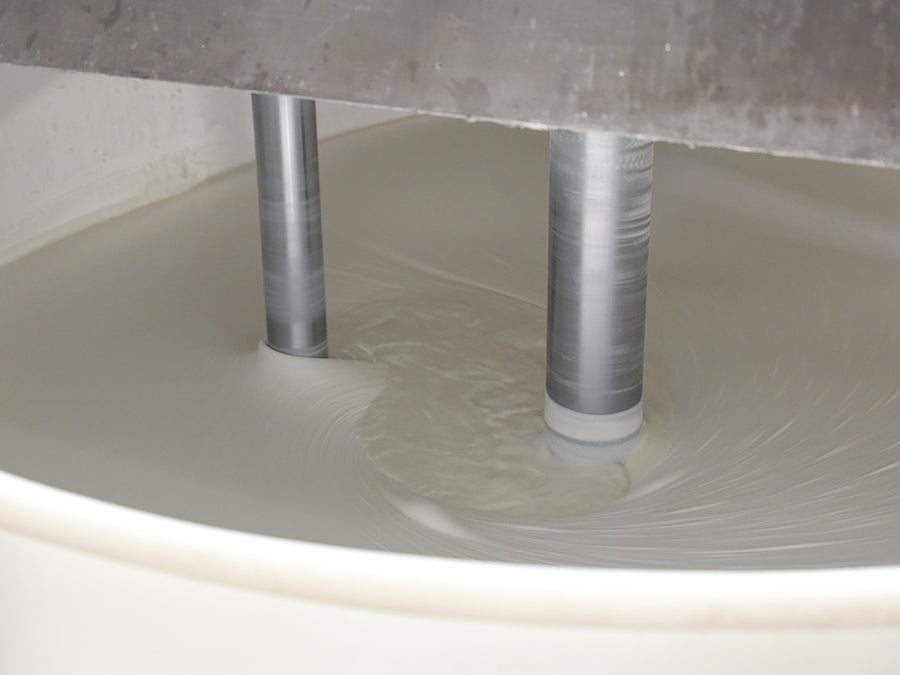 Viscous white liquid being mixed in a large tank by metal rods.
