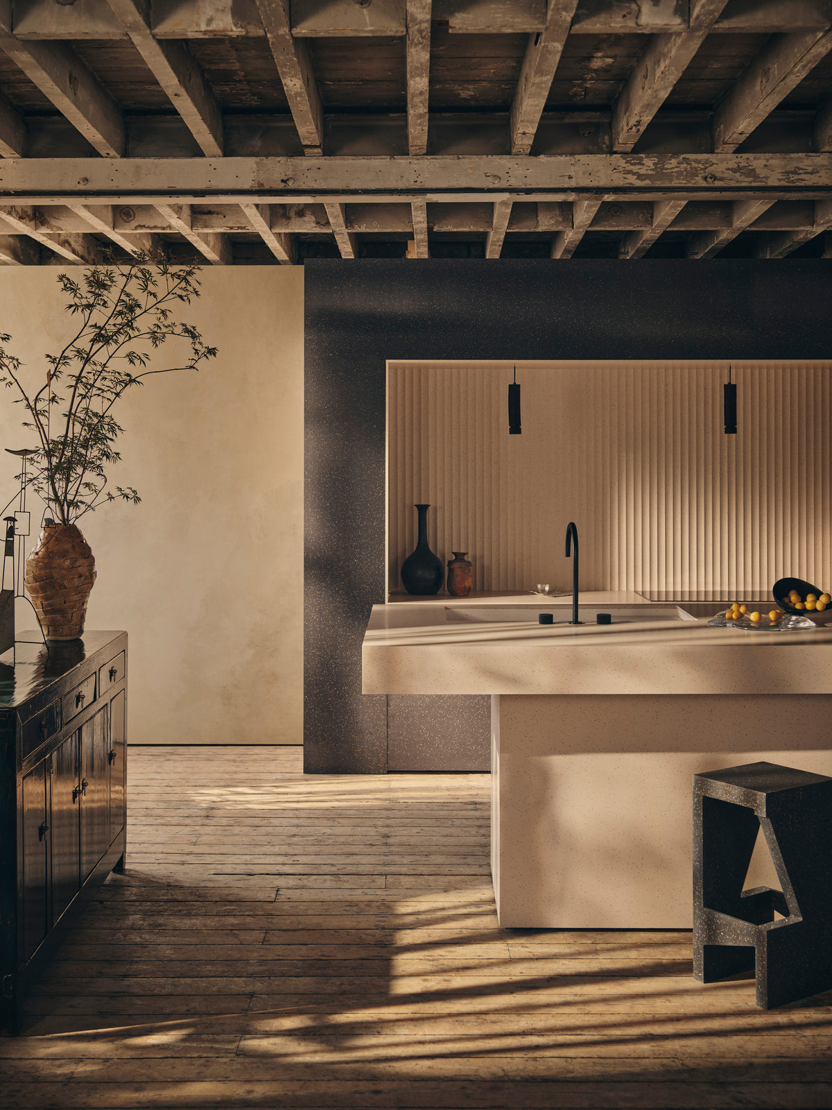A brown Elenite kitchen island with integrated sink set against a dark Elenite feature wall, with a fluted splashback, black tap, and rustic timber flooring.
