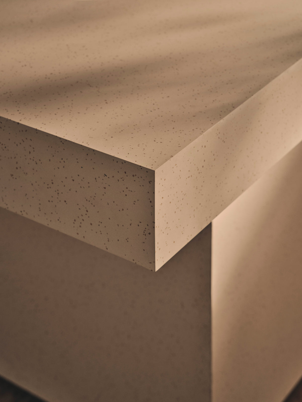 Close-up of a brown speckled solid surface worktop corner, showing the fine aggregate texture and clean mitre edge detail.