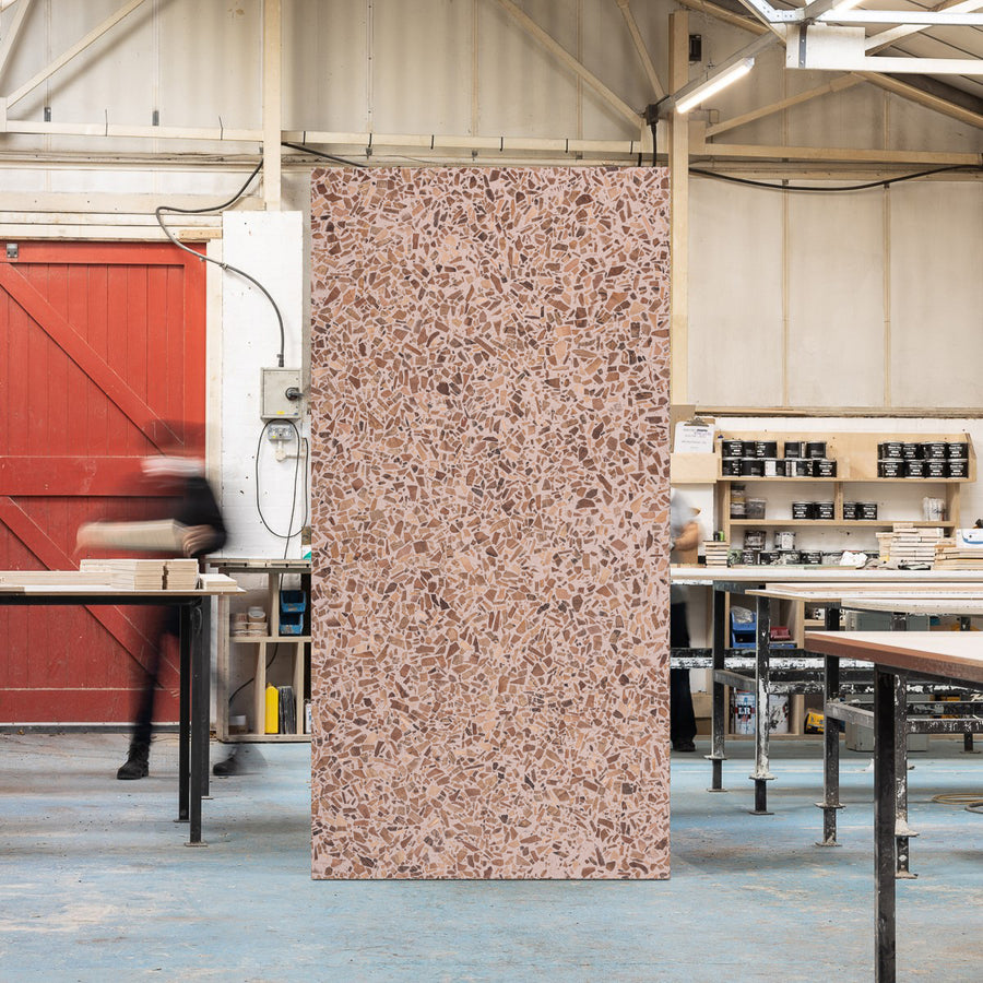 Full sized timber terrazzo sheet standing upright in a workshop setting, the surface is pink with London Plane wood chips.