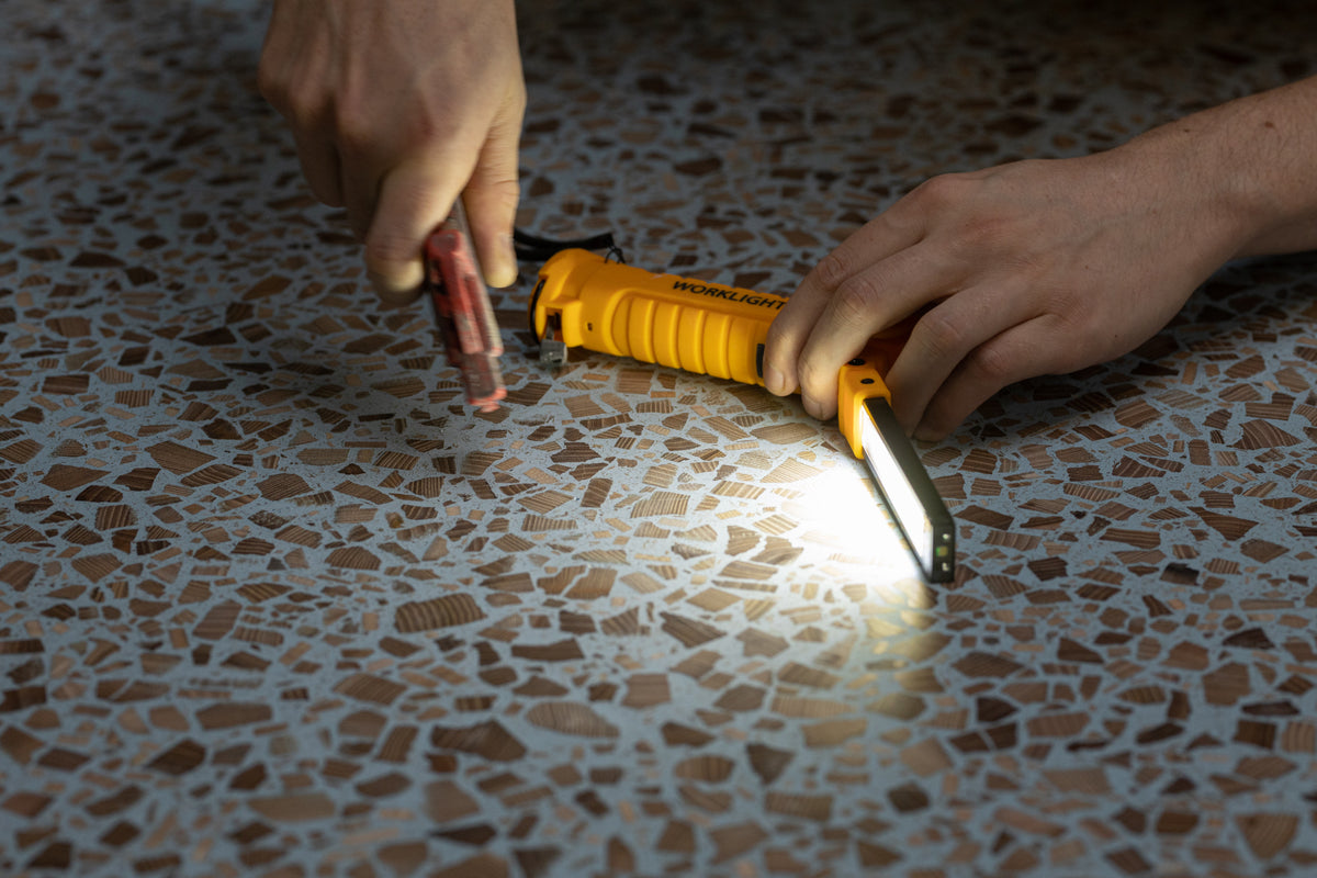 A person inspecting a blue wood terrazzo panel with a bright handheld light.