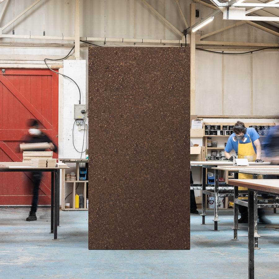 Full sized timber terrazzo sheet standing upright in a workshop setting, the surface is brown with Oak wood chips.