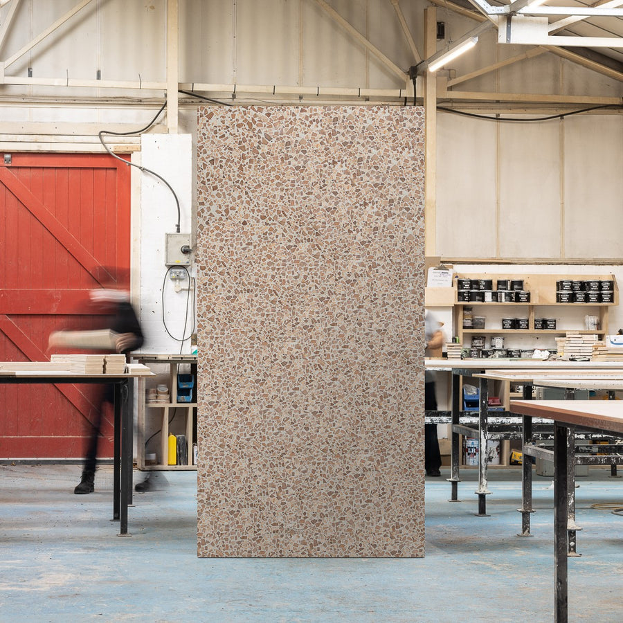 Full sized timber terrazzo sheet standing upright in a workshop setting, the surface is grey with Oak wood chips.